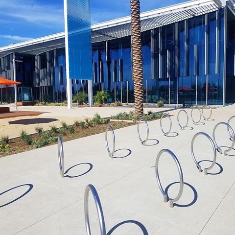 Gang’s all here: check out these rows of our Ring bike rack at @greatparkice. Ring is a simple circle hovering over the ground - it fits right in with this California-cool ice rink entrance.⁣⠀
⁣⠀
📷: @dsa_lighting⁣⠀⁣⠀
⁣⠀